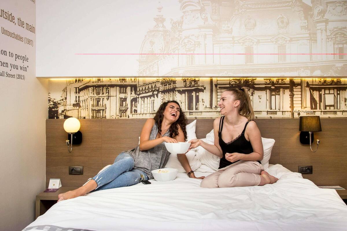 A hotel room with a bed, a nightstand, a lamp, and a wall with a mural.