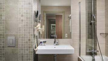 A bathroom with a sink, mirror, towel rack, shower, and a door leading to another room.