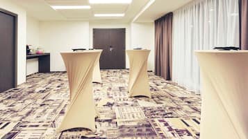 Una habitación de hotel con alfombra estampada, una puerta, una mesa con mantel y una ventana con cortinas.