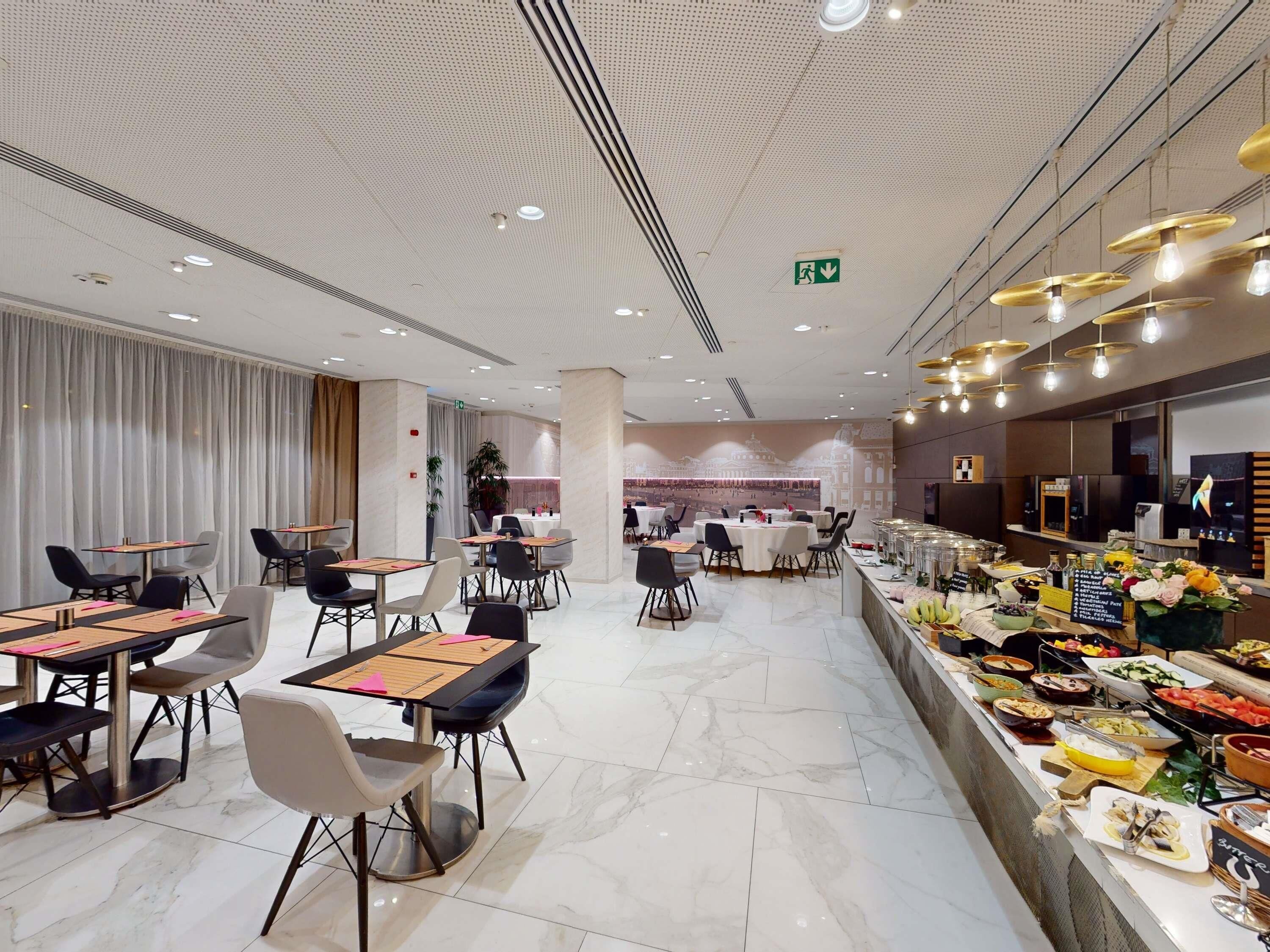 A modern dining area with tables and chairs, a buffet with various food items, and a decorative wall mural.