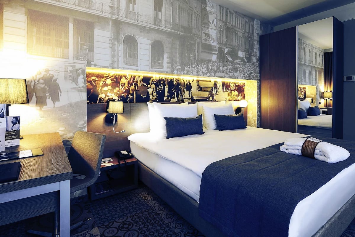 A hotel room with a large bed, bedside tables, a desk, and a chair.