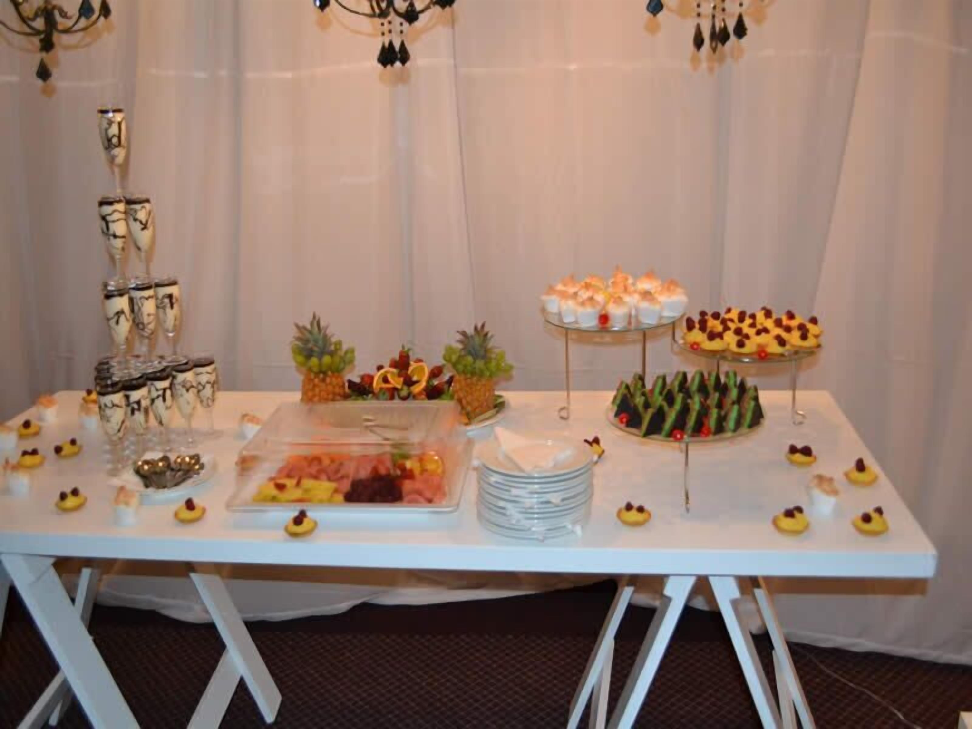 A buffet table with various food items and drinks, including fruit, desserts, and a glass display case.