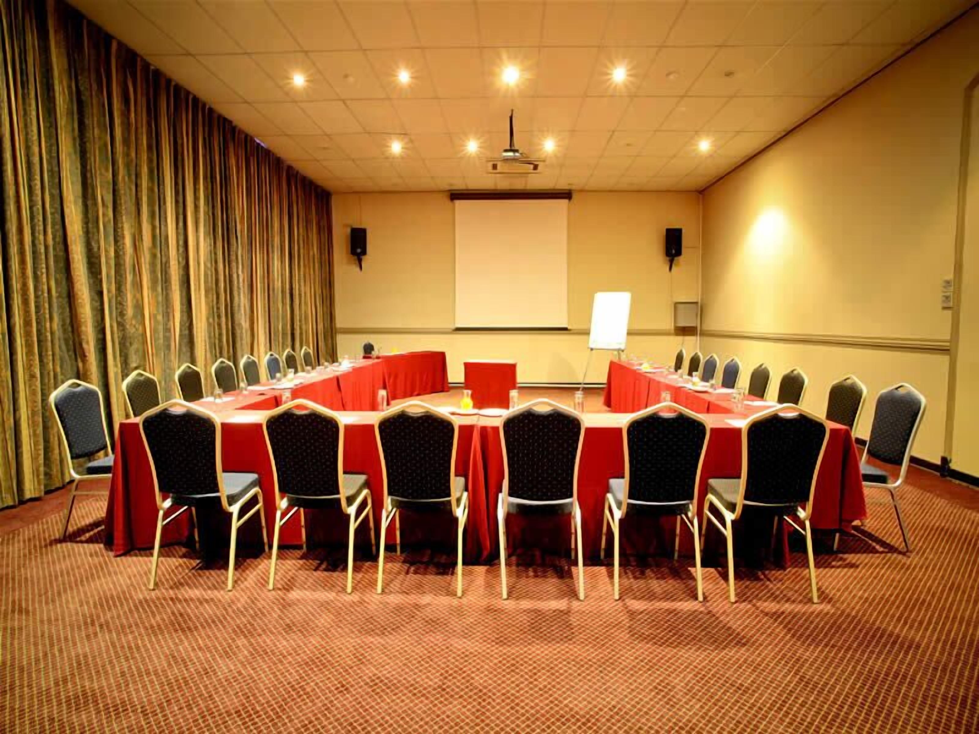 A conference room with multiple tables and chairs, a projector screen, and a whiteboard.