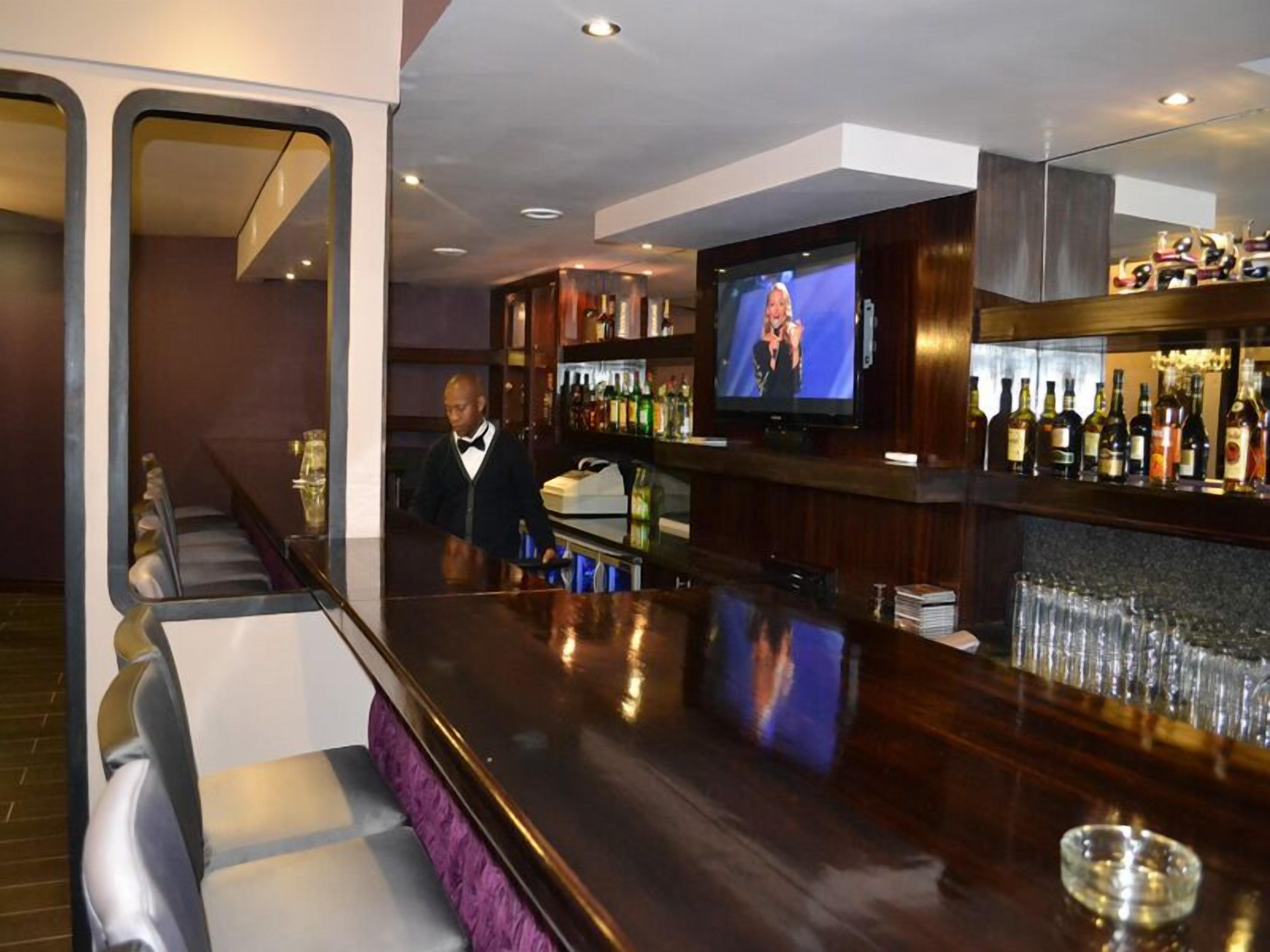 A bar area with a television, bar stools, and a bartender.