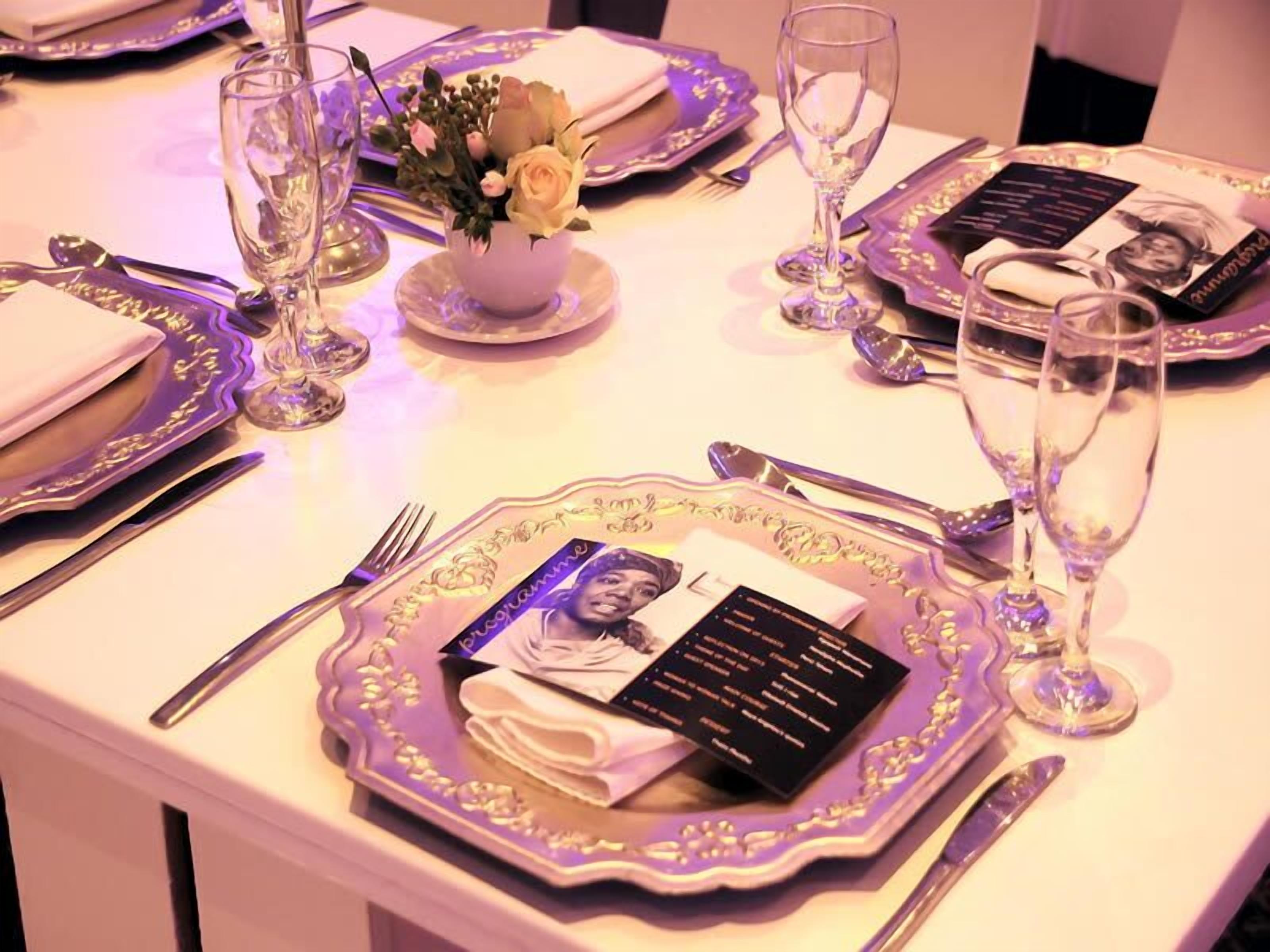 A table set for a formal dinner with a menu, a vase with flowers, and a glass of champagne.