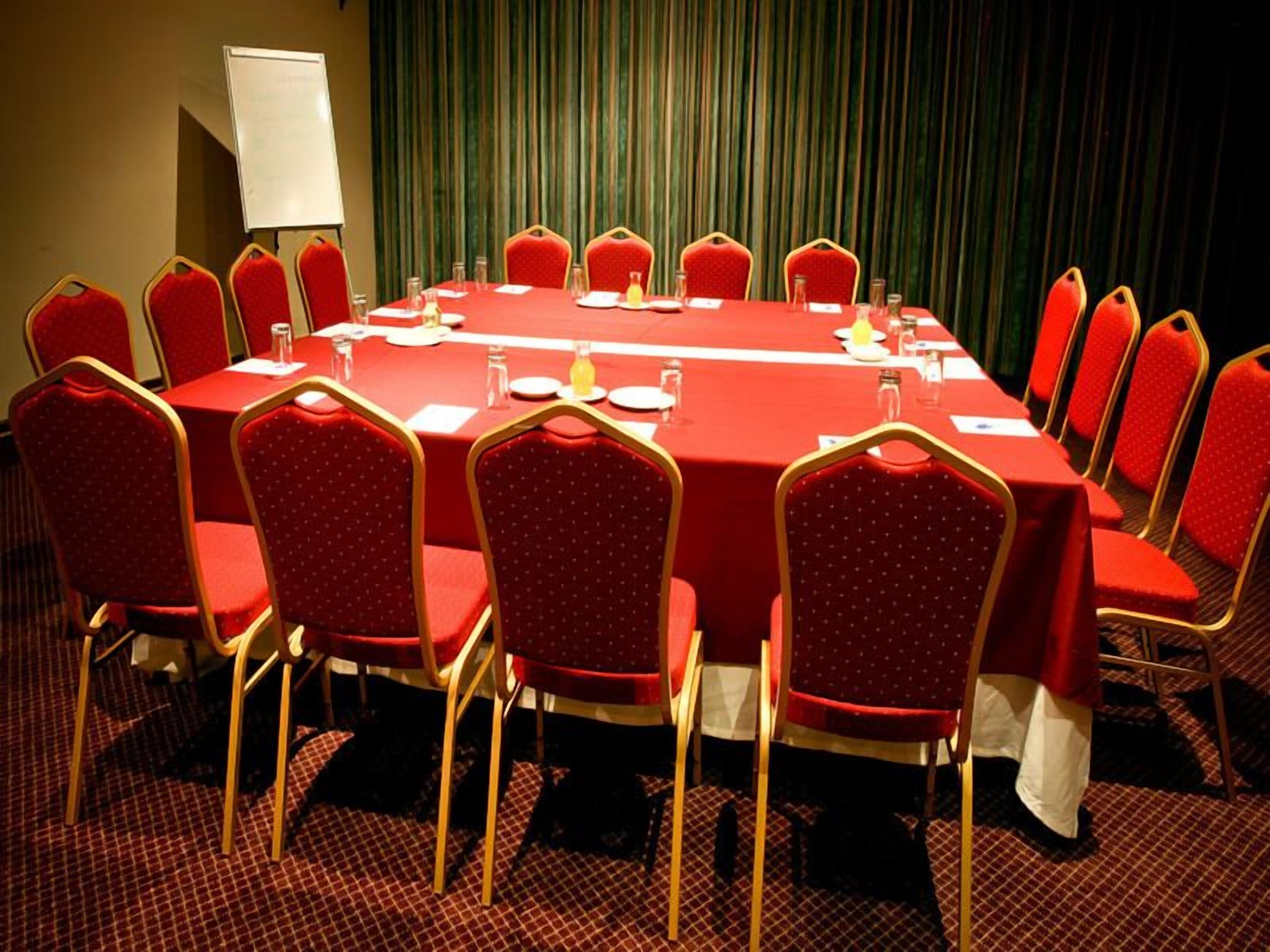 A conference room with a long table, red chairs, and a whiteboard.