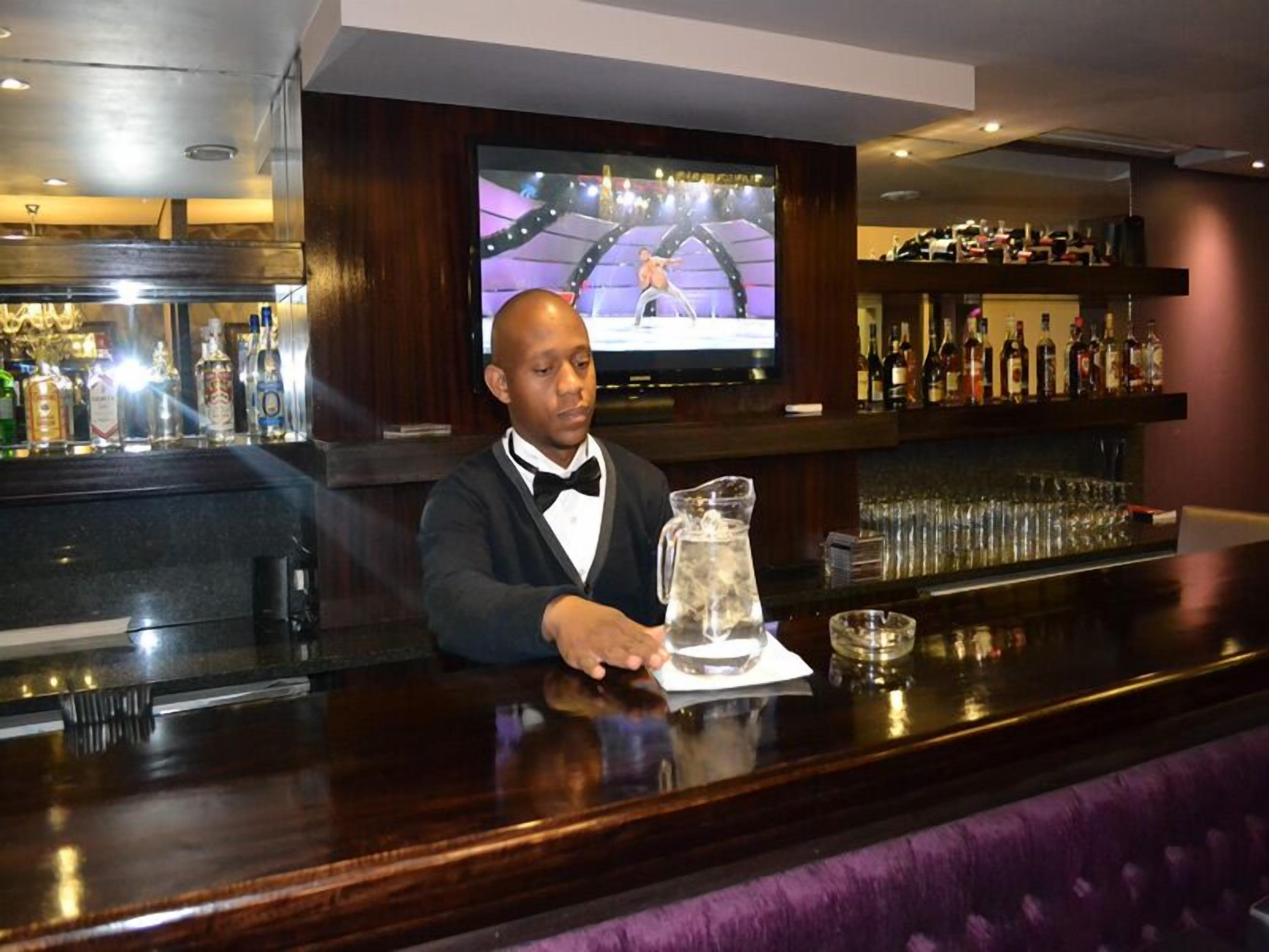 Zona de bar con un cantinero, una pantalla de televisión y una barra repleta de botellas.