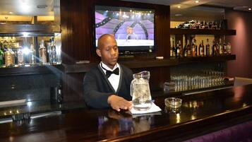 A bar area with a bartender, a television screen, and a bar stocked with various bottles.