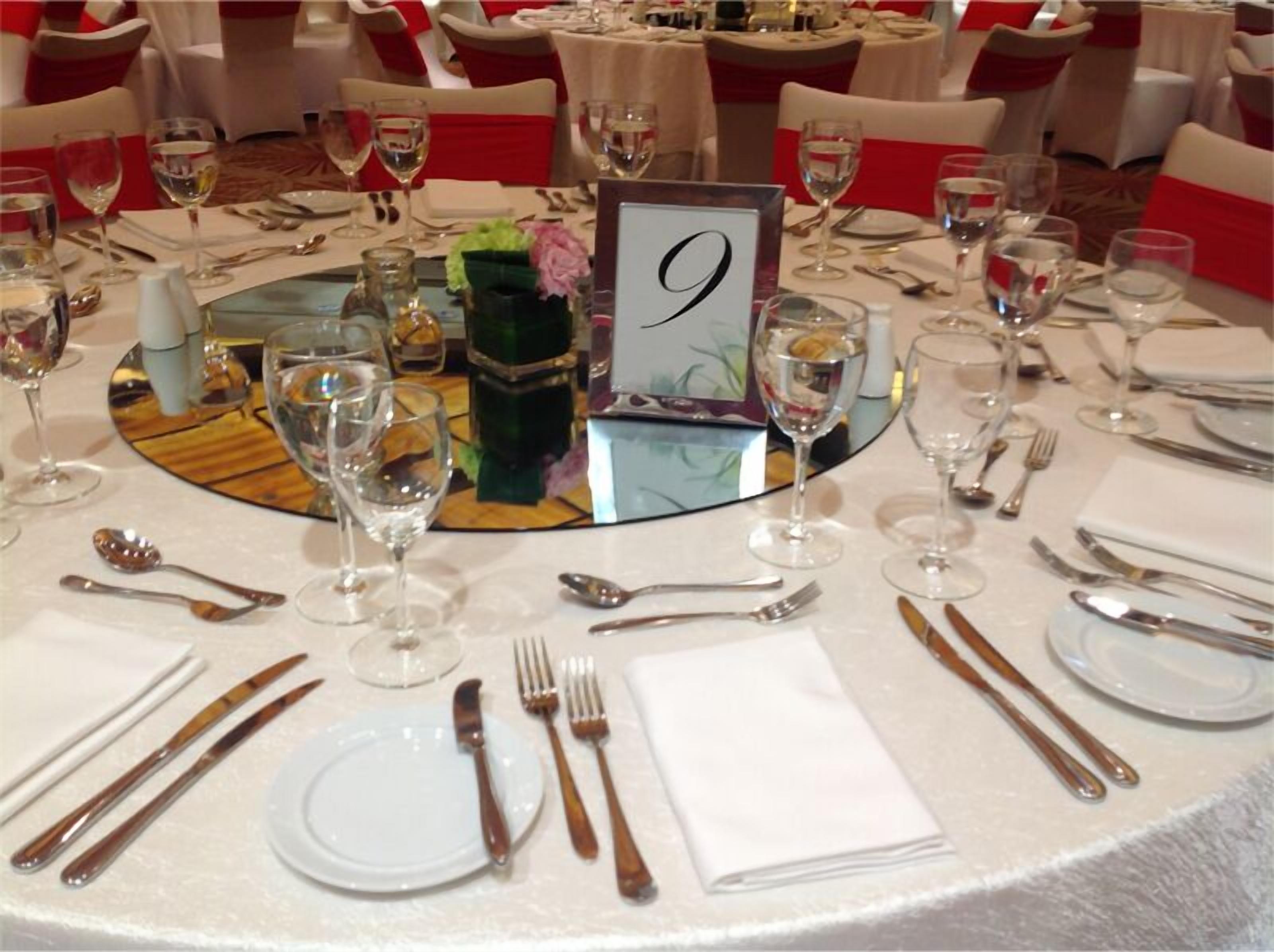 A round dining table with a number 9 sign, white tablecloth, and red sashes on chairs.