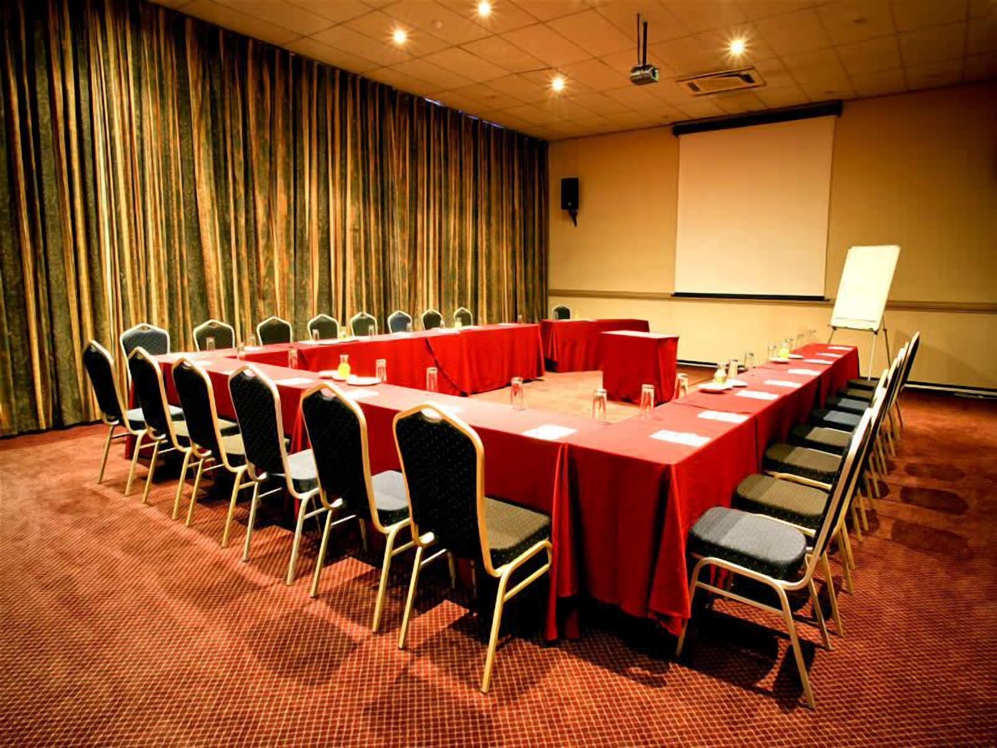 A conference room with a long table, chairs, a projector screen, and a whiteboard.