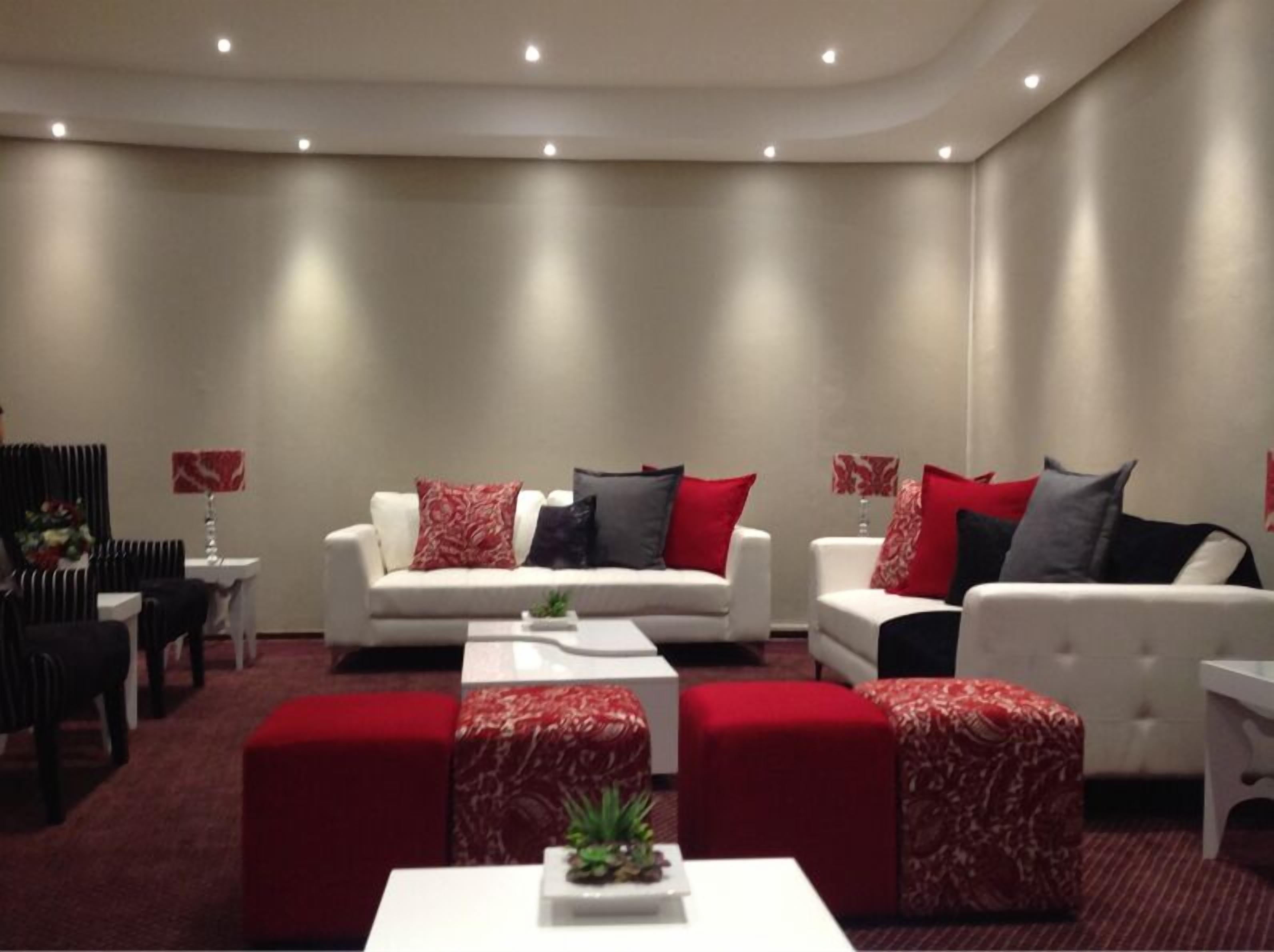 Una sala de estar moderna con dos sofás blancos, cojines rojos y grises, una mesa de centro y otomanas rojas.