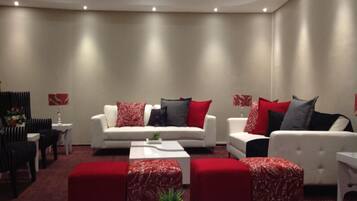 Una sala de estar moderna con dos sofás blancos, cojines rojos y grises, una mesa de centro y otomanas rojas.