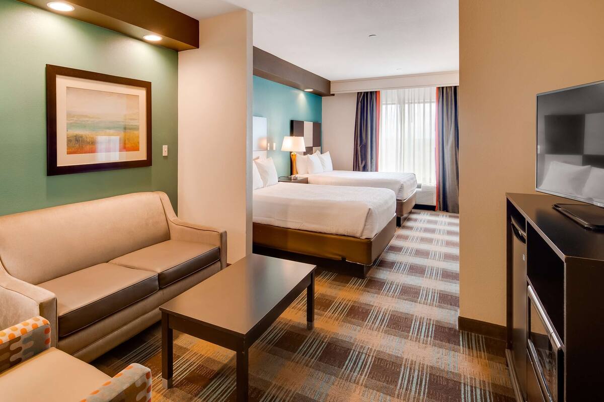 A hotel room with a sofa, a small table, a TV, and two beds.