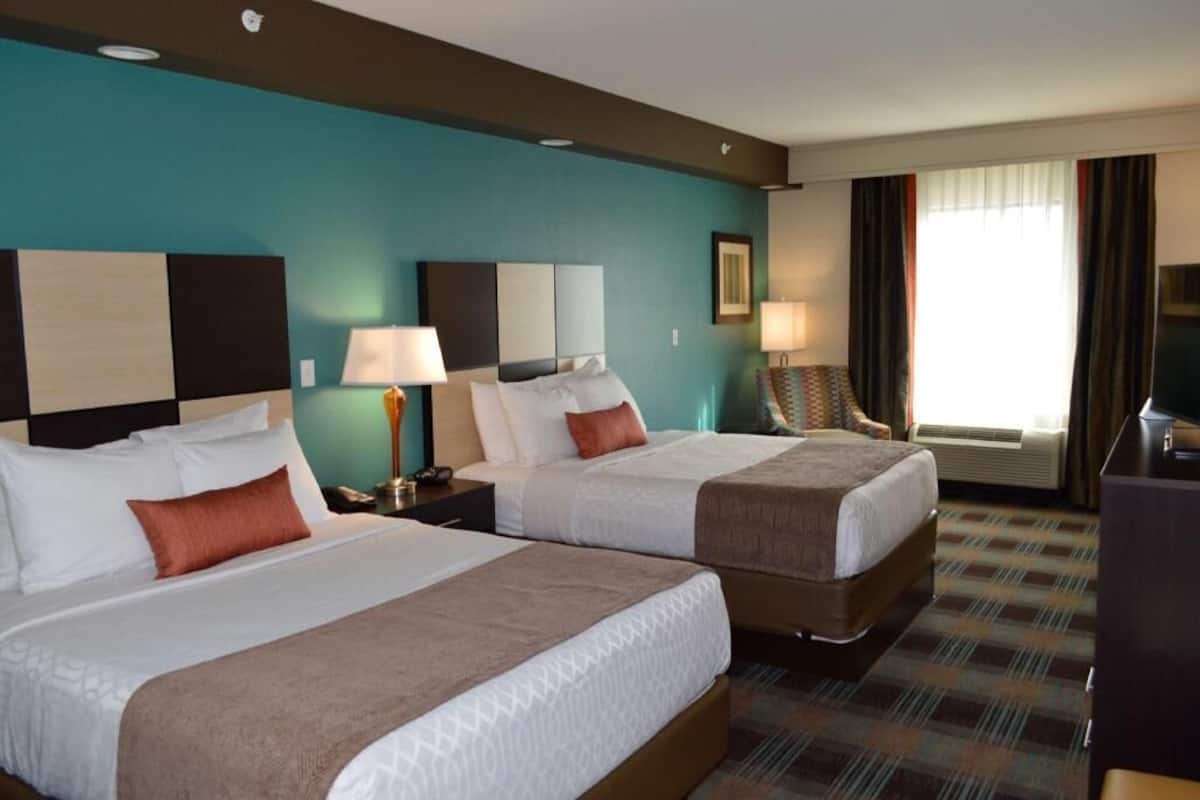 A hotel room with two beds, a desk, a chair, a TV, and a window with curtains.