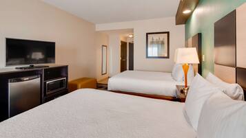 A hotel room with two beds, a TV, a microwave, and a desk.