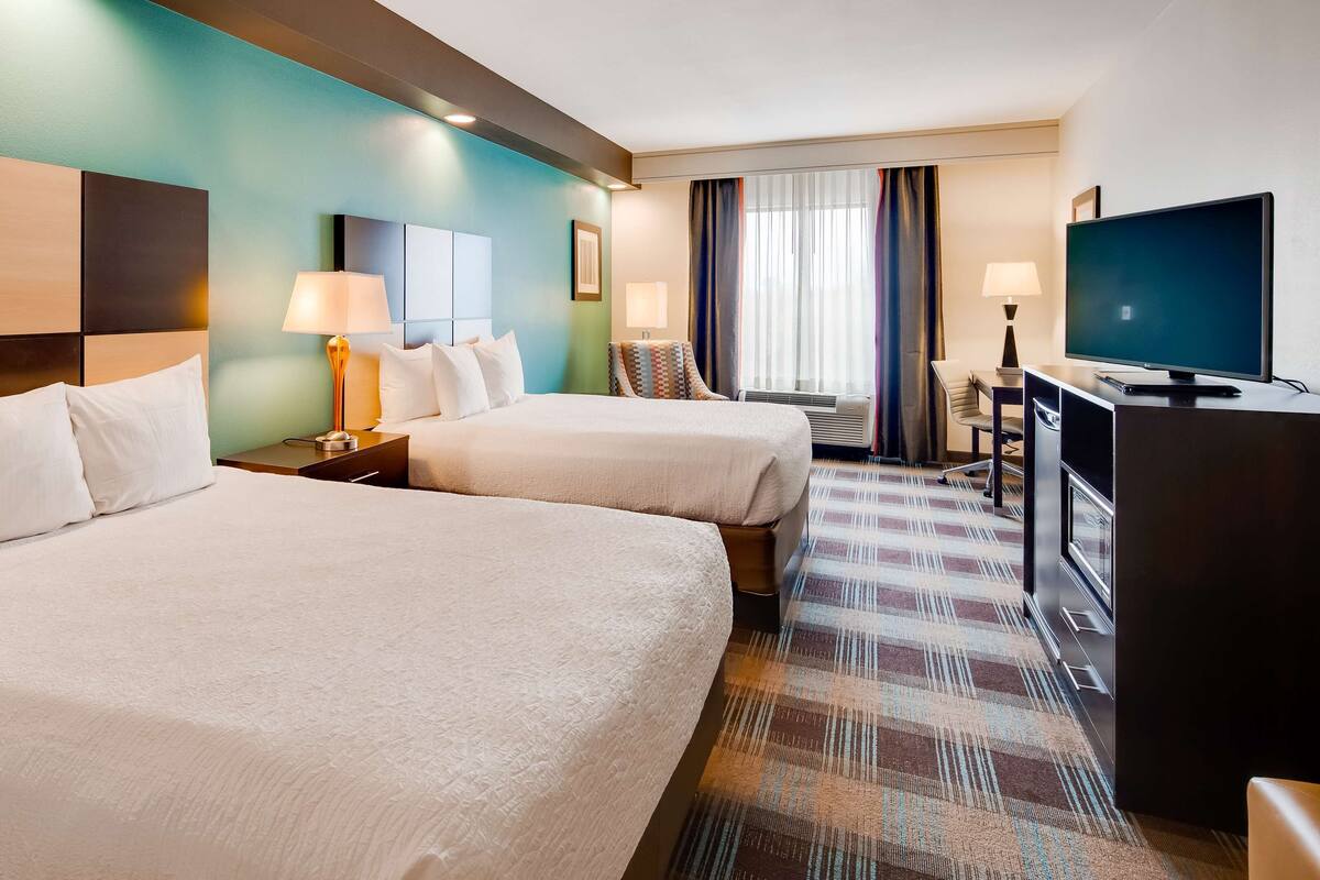 A hotel room with two beds, a TV, and a desk with a chair.
