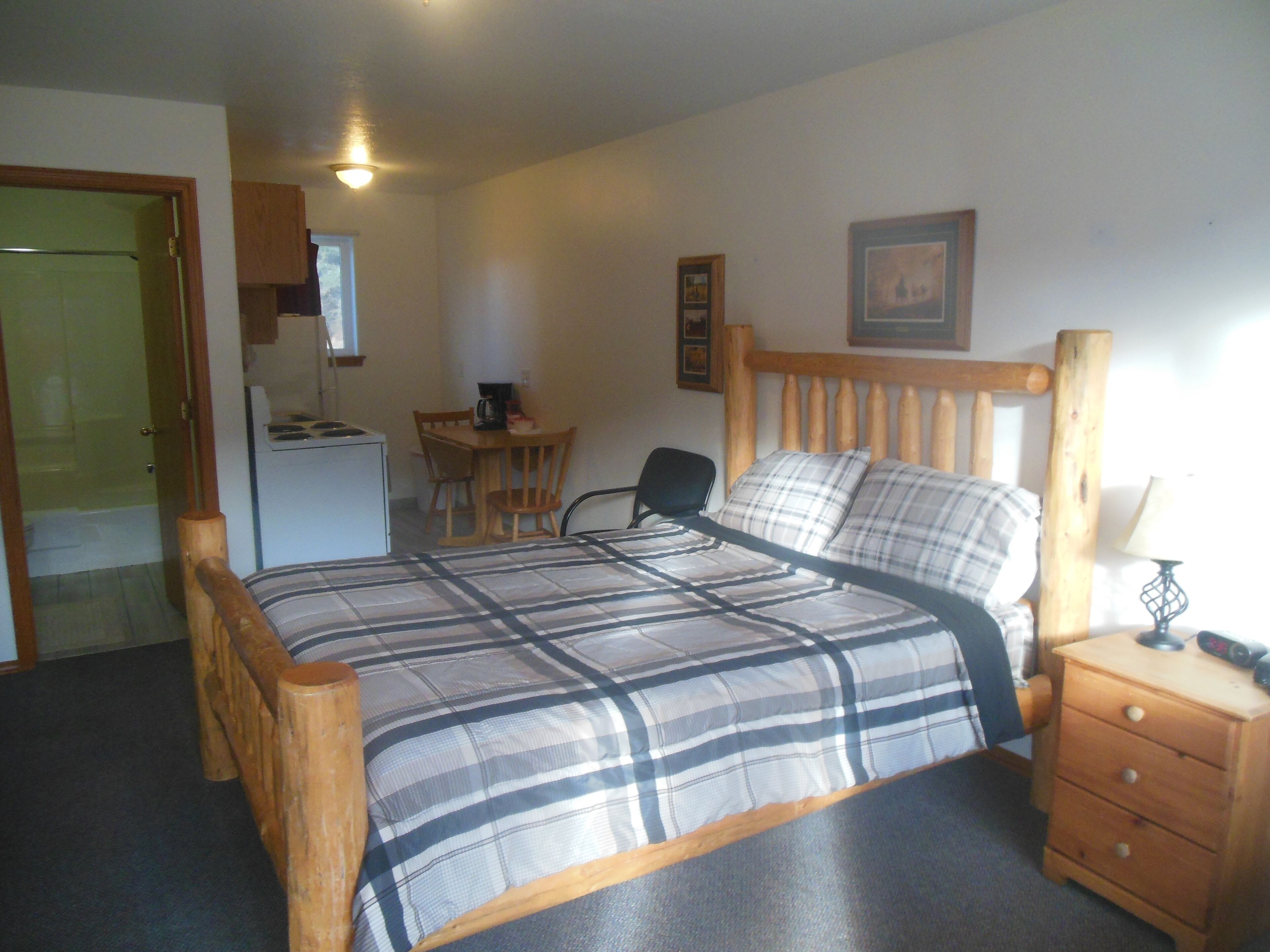 A bedroom with a bed, a desk, a chair, a dresser, and a small kitchenette.