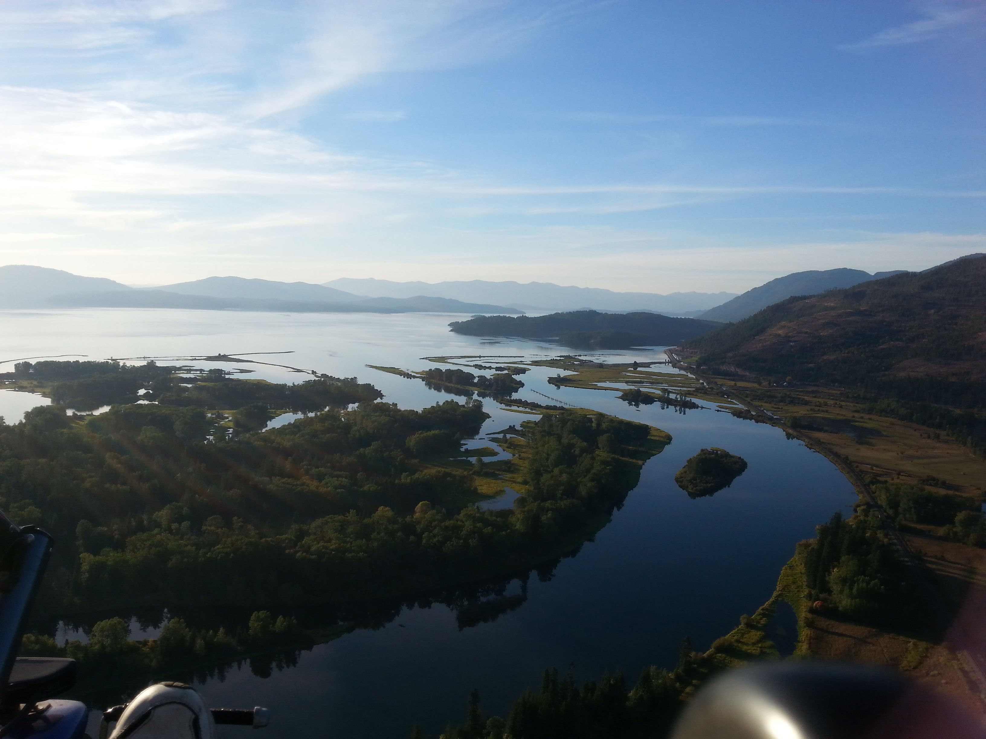 A panoramic view of a lake surrounded by hills and trees.