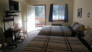 A room with two beds, a desk with a chair, a television, and a window with curtains.