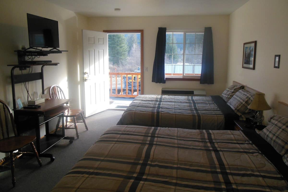 A room with two beds, a desk with a chair, a television, and a window with curtains.