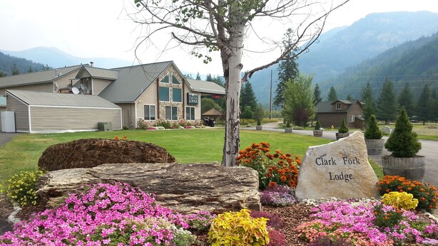 A lodge with a stone sign, surrounded by colorful flower beds and a large rock.