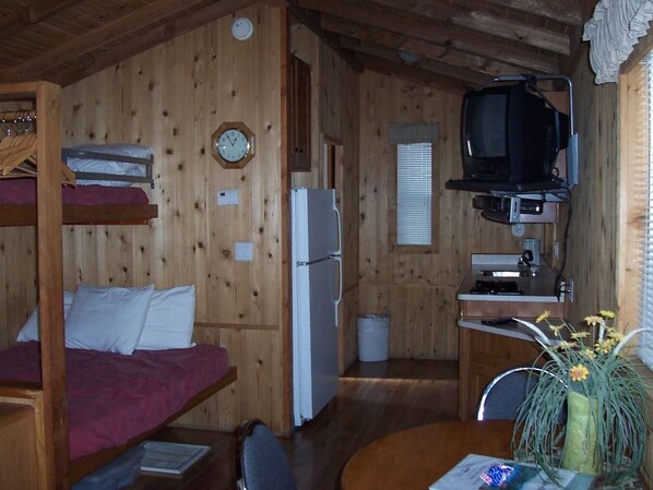 Una cabaña con literas, un refrigerador, un televisor y una pequeña cocina.