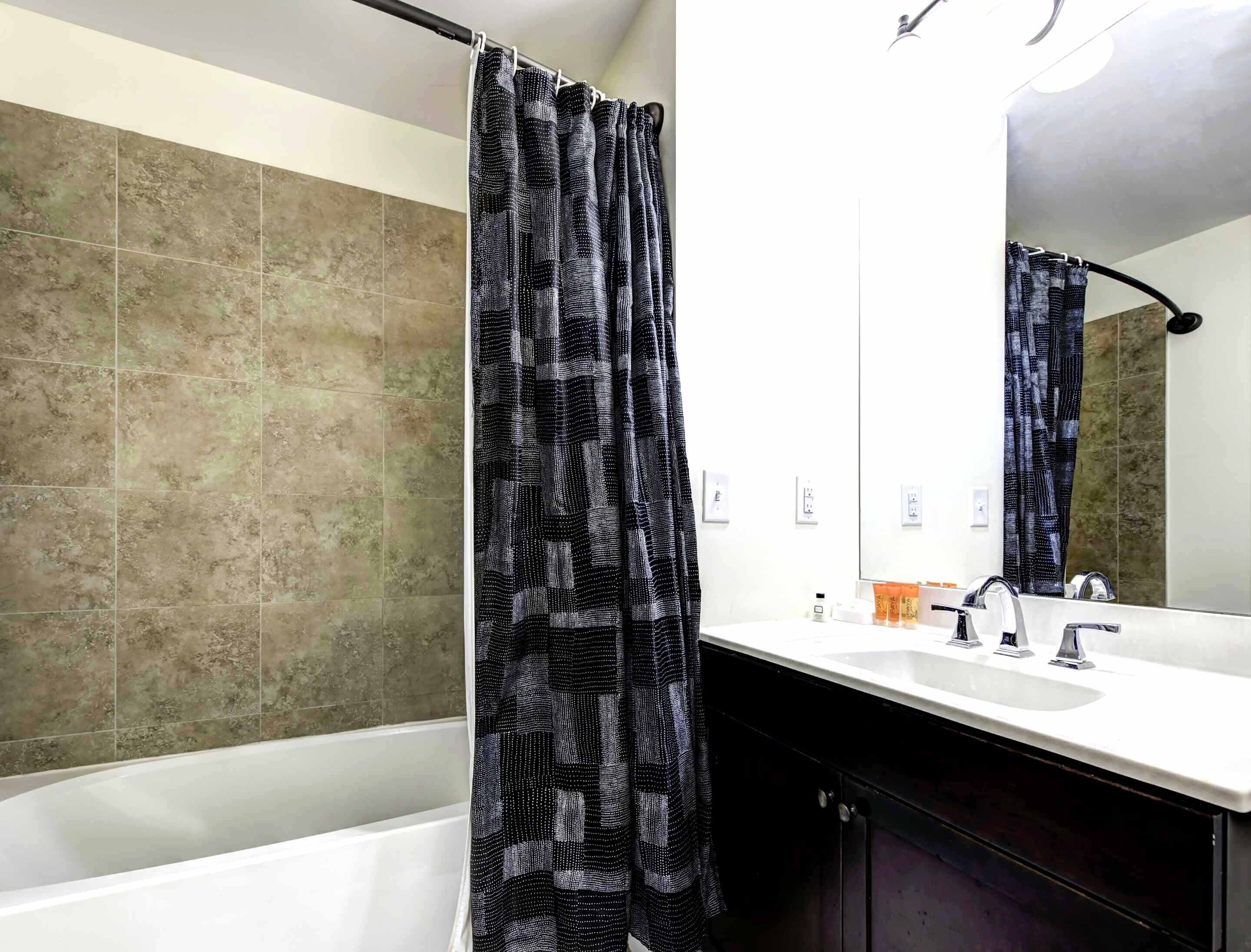 Une salle de bain avec une baignoire, un rideau de douche, un lavabo et un miroir.