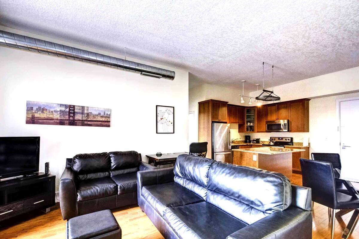 Una sala de estar moderna con un sofá de cuero negro, un televisor de pantalla plana y una mesa de comedor de madera.