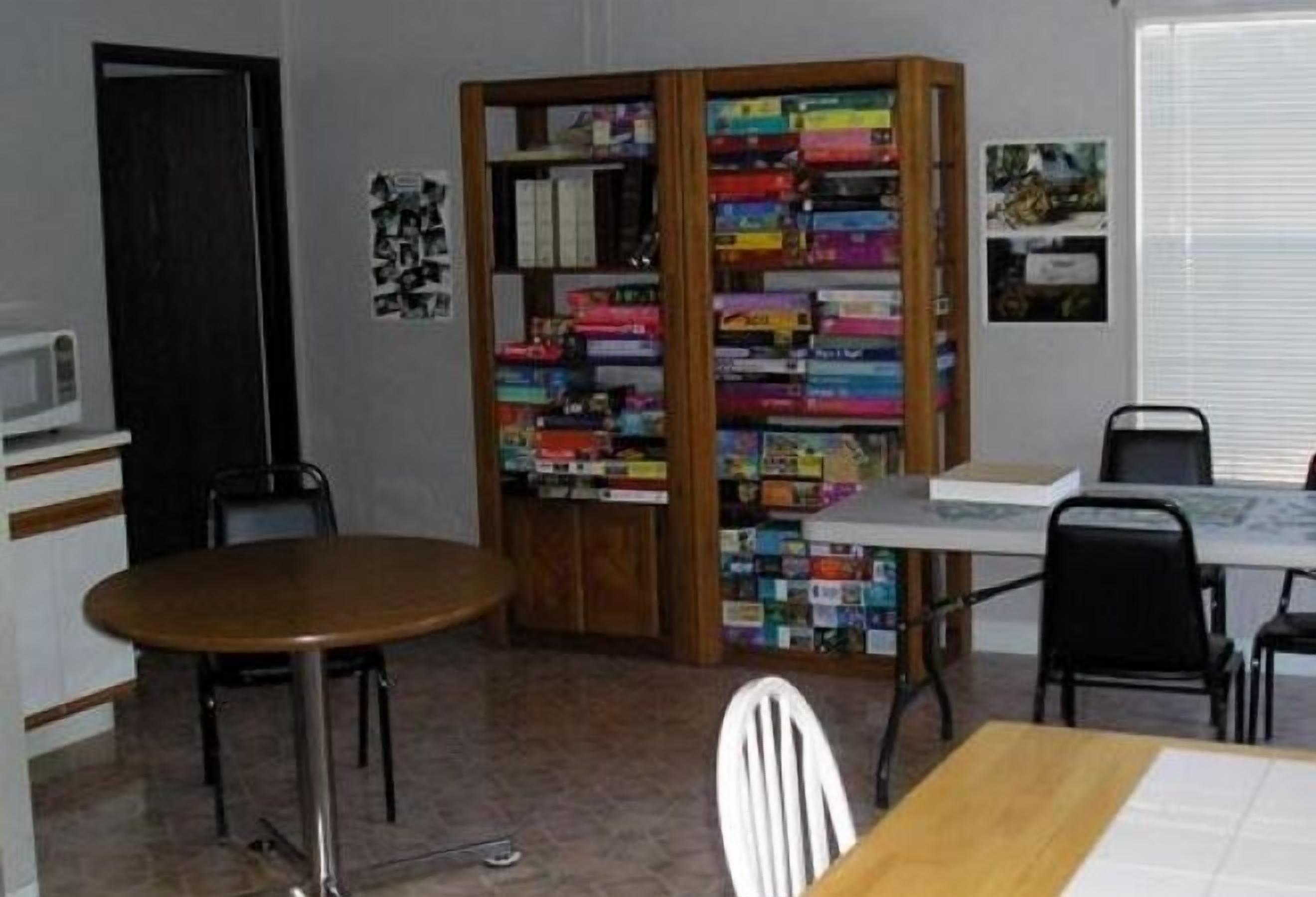 A room with a wooden table, a bookshelf filled with books, a white chair, and a small white desk with a chair.