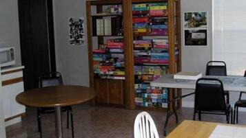 A room with a wooden table, a bookshelf filled with books, a white chair, and a small white desk with a chair.