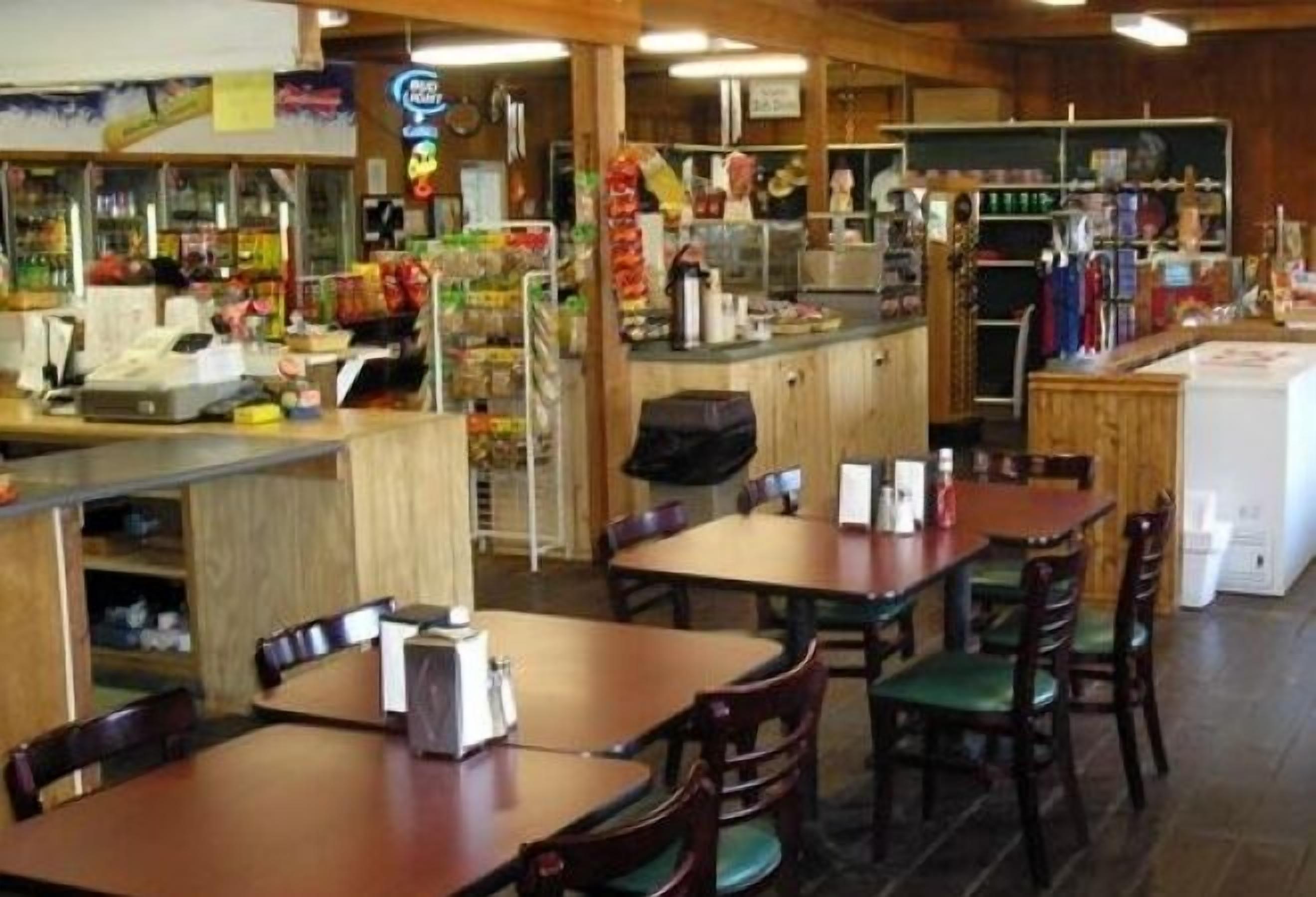 A restaurant interior with wooden tables and chairs, a counter with various food items, and a visible menu board.