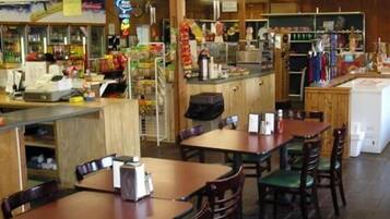 A restaurant interior with wooden tables and chairs, a counter with various food items, and a visible menu board.