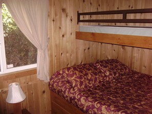 A bunk bed with a patterned bedspread, a window with curtains, and a lamp on the floor.