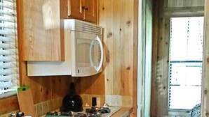A wooden cabin-style kitchen with a built-in microwave, a sink, and a stove. - Snowflower RV Resort (Emigrant Gap)