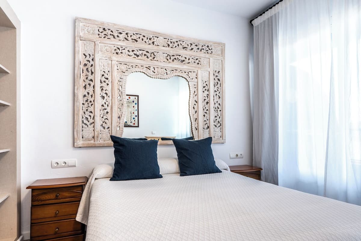 A hotel room with a large bed, two nightstands, a wooden dresser, and a decorative mirror with intricate carvings.