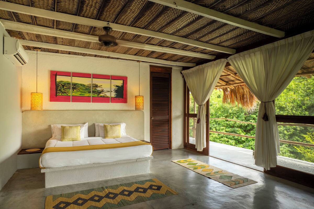 Un dormitorio con cama, un cuadro, una ventana con cortinas y vistas a zonas verdes.