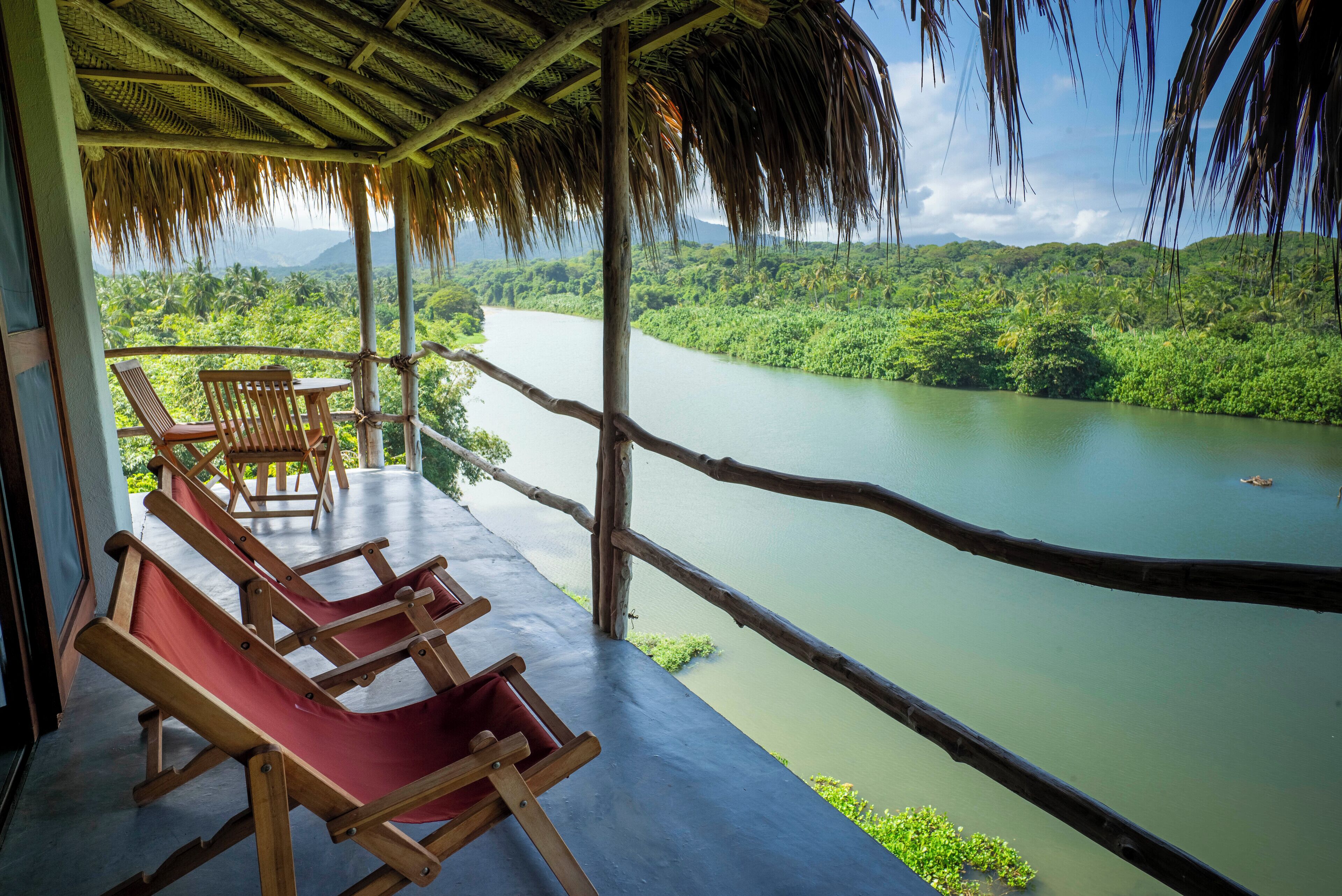 A wooden deck with lounge chairs overlooking a river and lush greenery.