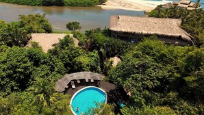 Un resort tropical con piscina, playa y edificios de techo de paja.