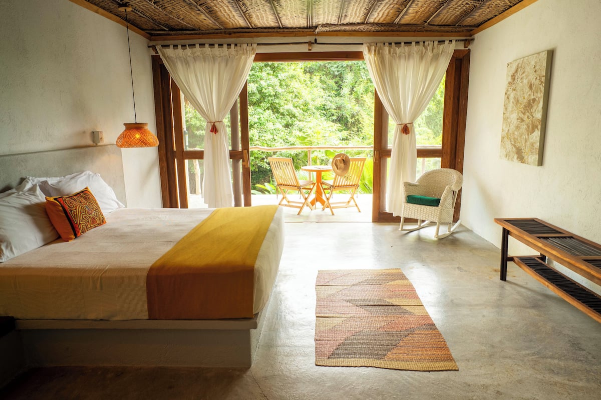 Un dormitorio con cama, un banco de madera, una mecedora y una pequeña mesa con sillas.