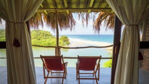 Una habitación con dos sillas de madera orientadas hacia una vista a la playa, a través de una estructura de techo de paja.