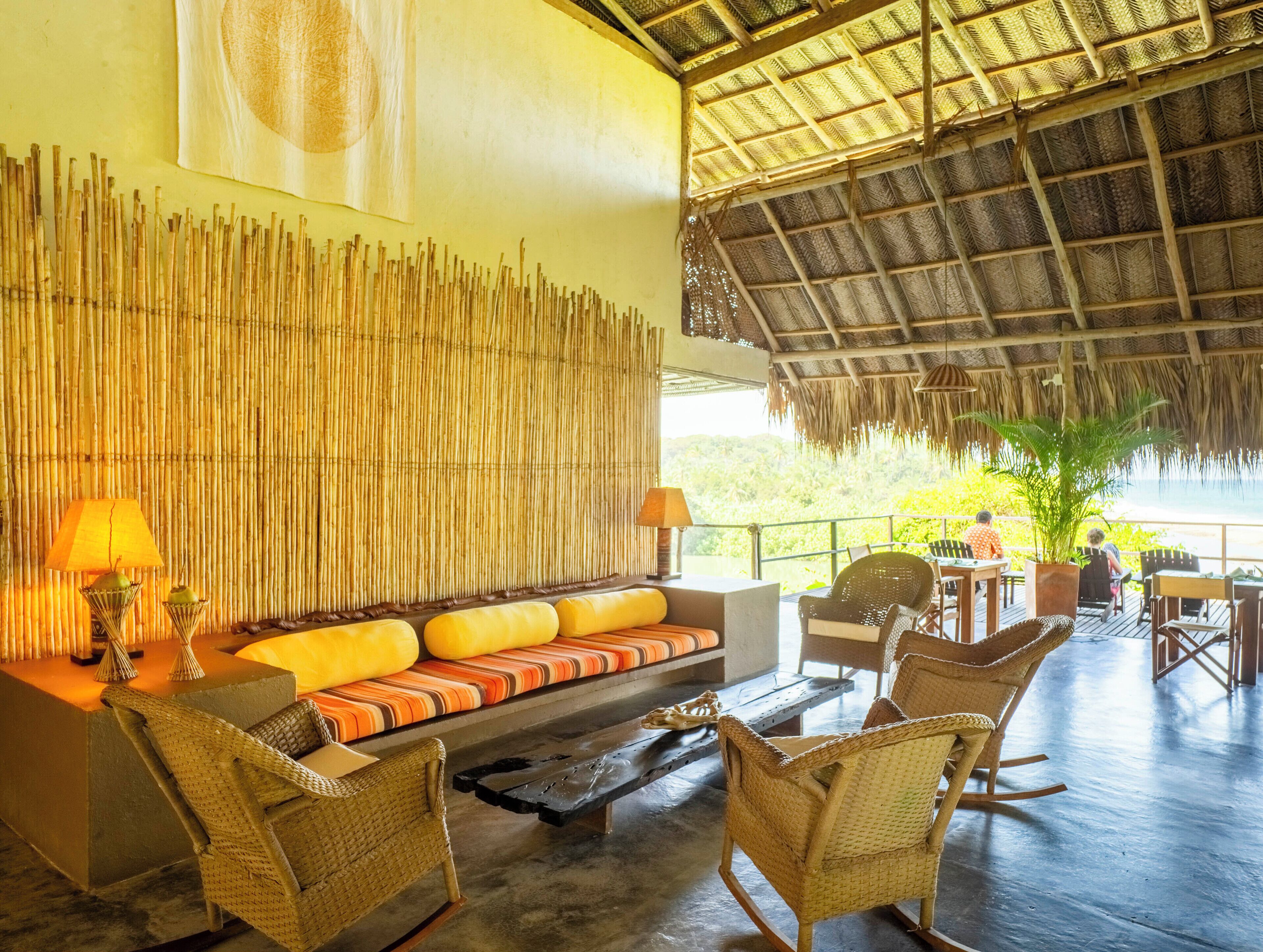 A lounge area with a thatched roof, bamboo wall, and a sofa with cushions.