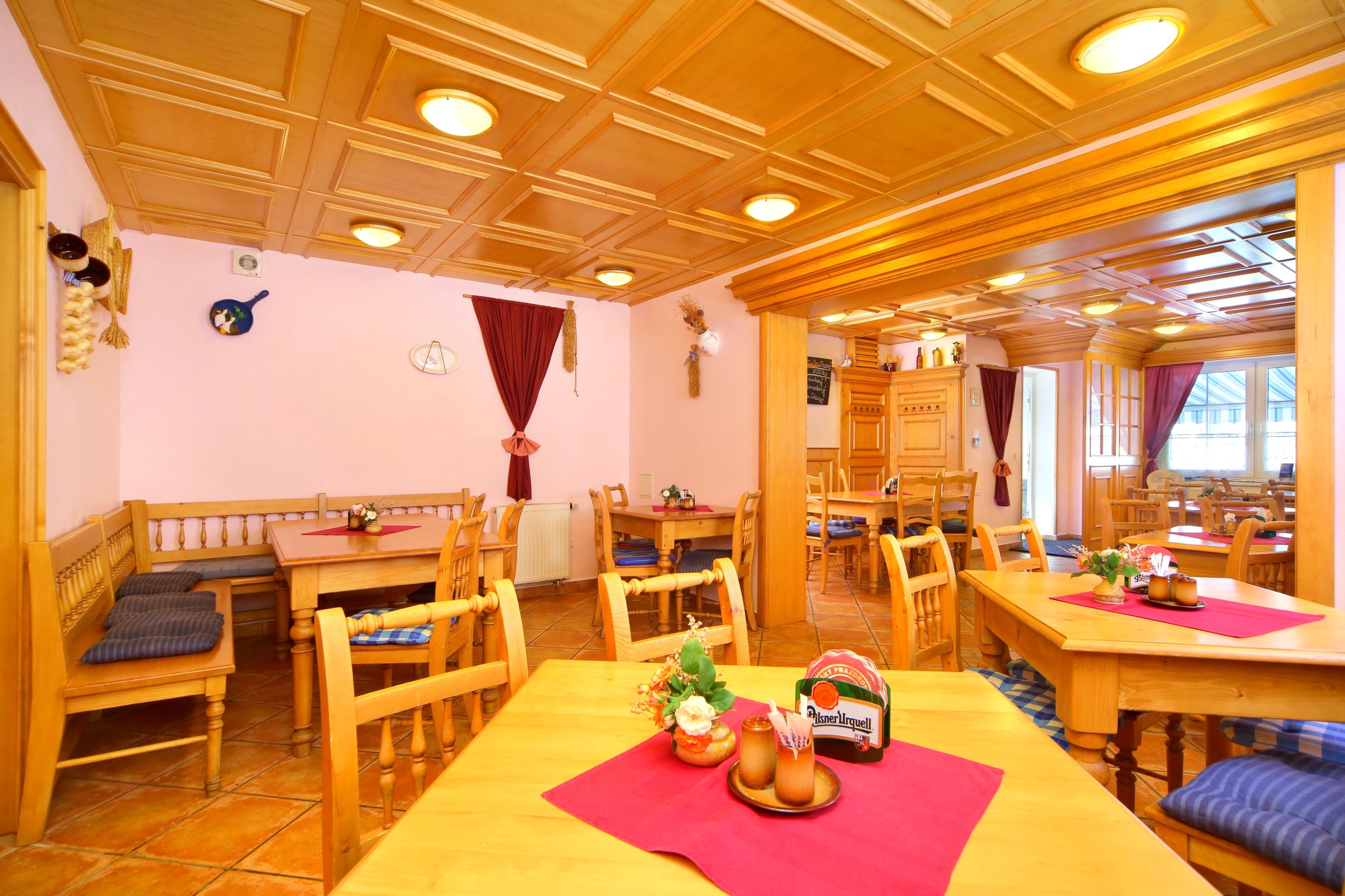 A dining area with wooden furniture, a red table runner, and a bottle of Pilsner Urquell beer.