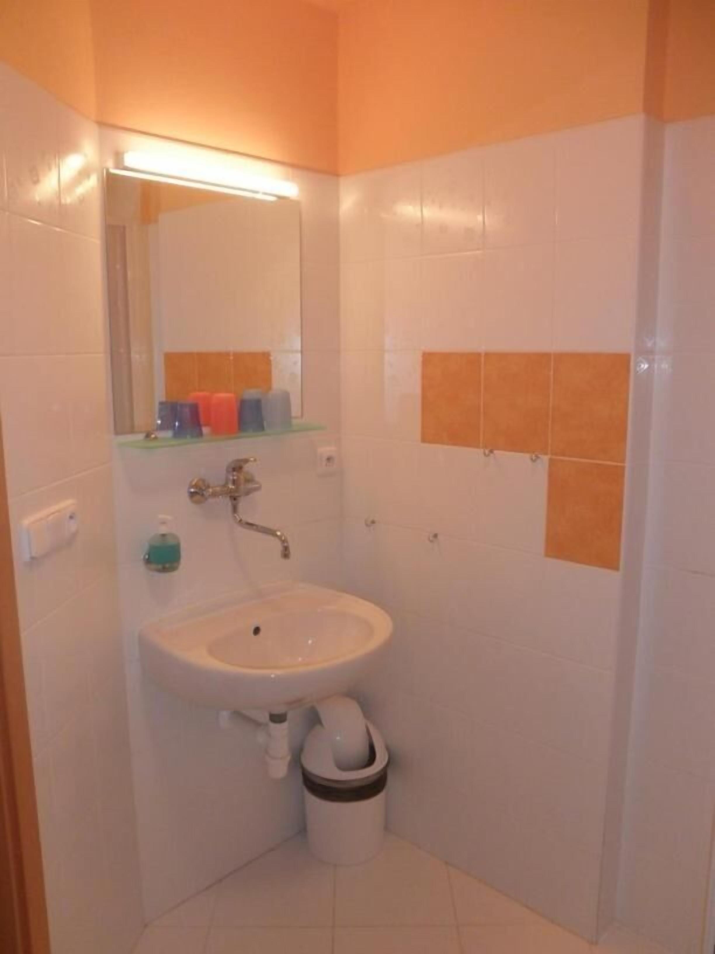 Un baño con un lavamanos blanco, un espejo y una pared con azulejos anaranjados.