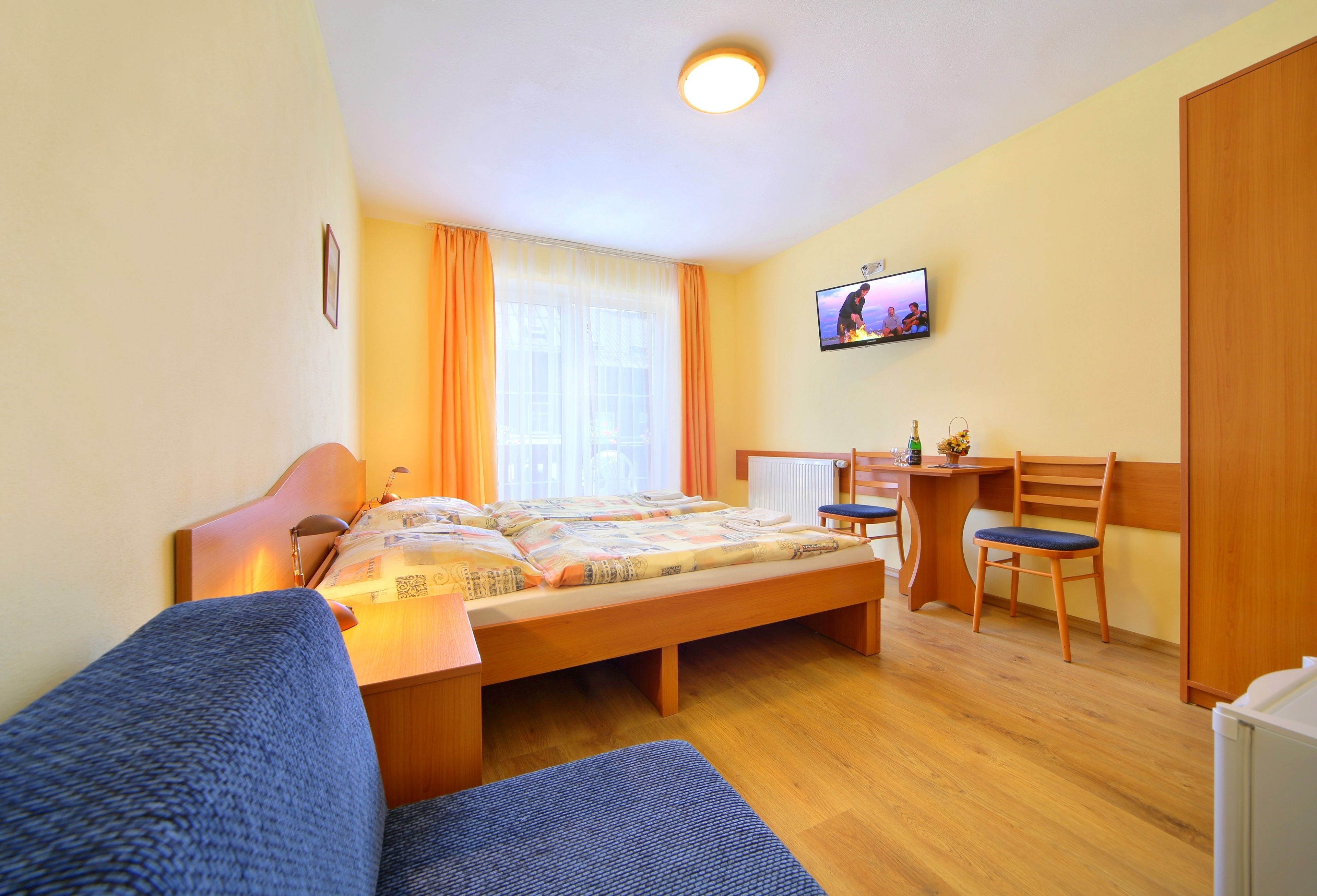 A bedroom with a bed, a desk, a chair, a television, and a window with curtains.