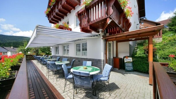 Un patio al aire libre con mesas y sillas, una terraza de madera y un edificio con balcones decorados con flores.