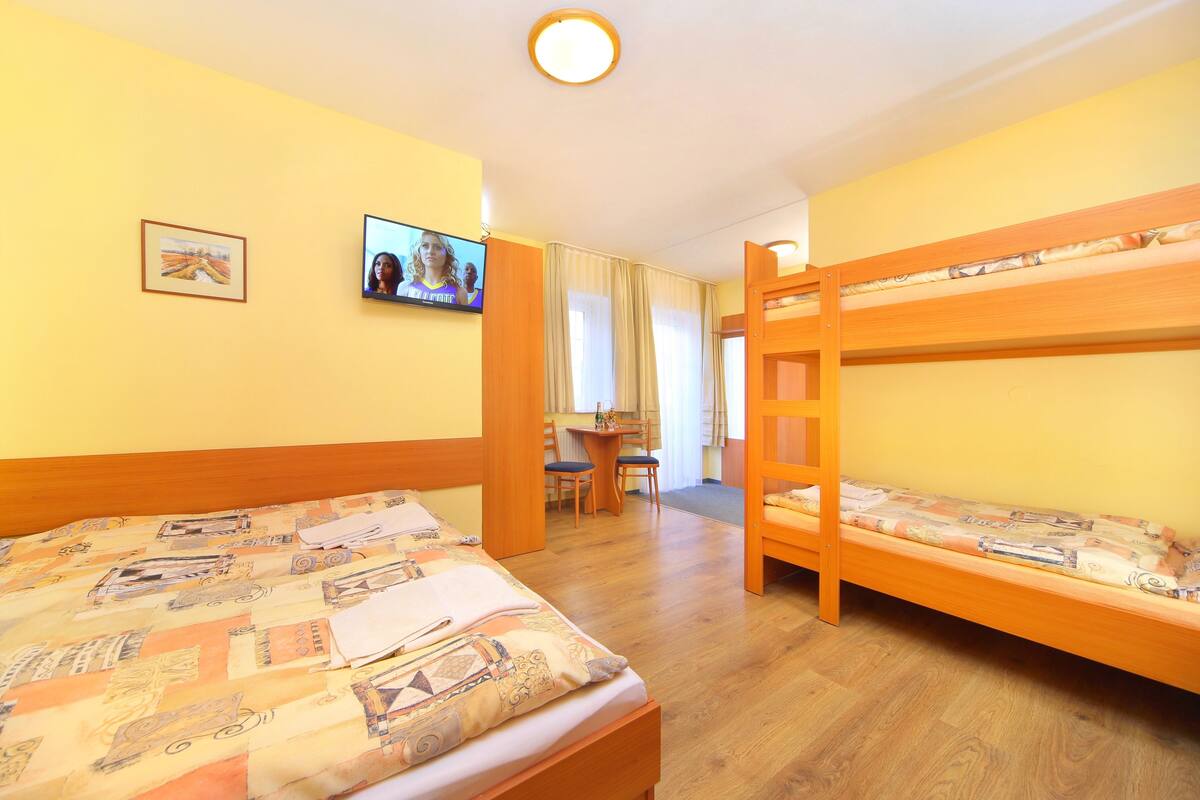 A room with two bunk beds, a television, a desk with a chair, and a window with curtains.