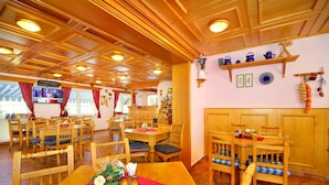 Un restaurante con mobiliario de madera, una pantalla de televisión y un estante con utensilios de cocina.