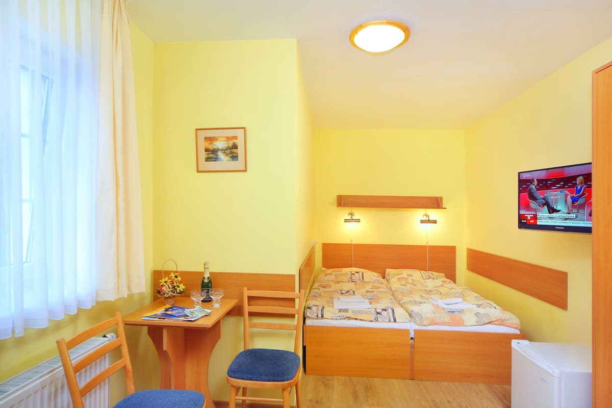 A room with a bed, a desk, a chair, a TV, and a window with curtains.