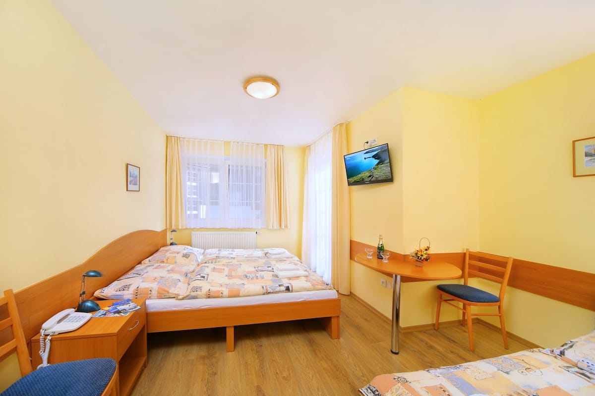A hotel room with a bed, a desk, a chair, a TV, and a window with curtains.