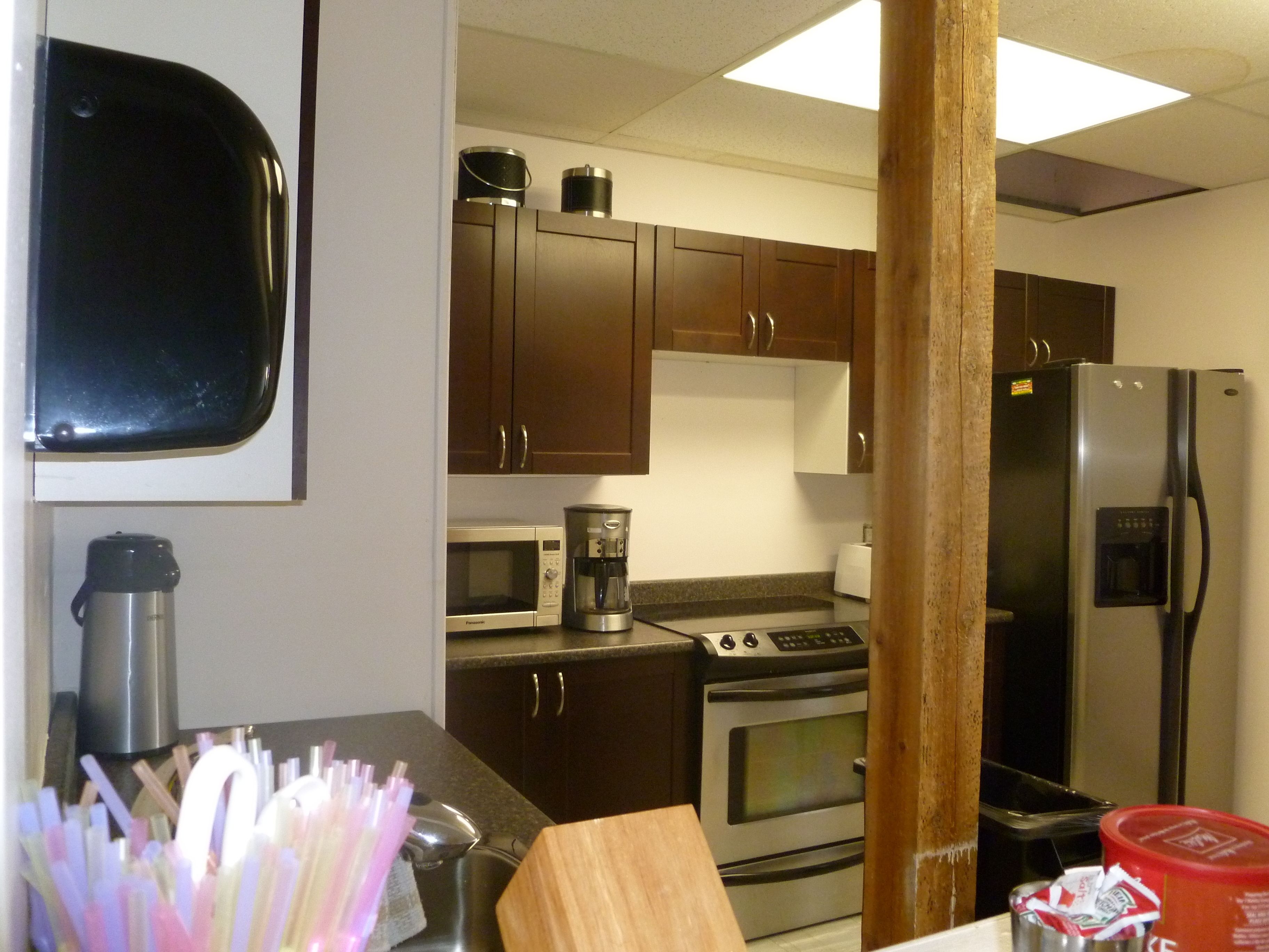 A kitchen with dark wooden cabinets, a stainless steel refrigerator, a microwave, a coffee maker, and a toaster.